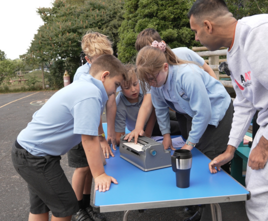 Children learning to use a Braille writer outdoors